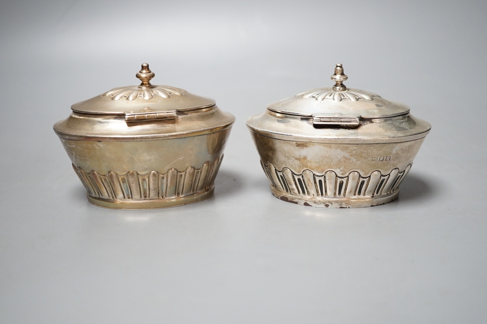 A matched pair of early 20th century silver oval tea caddies, London, 1908 & 191, width 10.5cm and two early 20th century silver leaf caddy spoons, one Britannia standard.